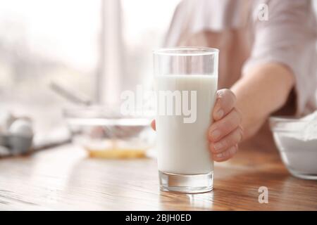 Alte Frau hält Glas mit frischer Milch auf dem Tisch Stockfoto