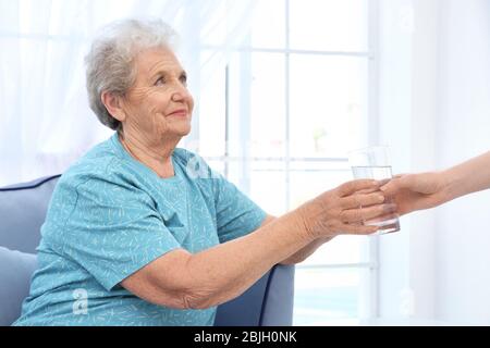 Junge Dame, die älteren Frauen ein Glas Wasser gibt. Konzept der Pflege Stockfoto