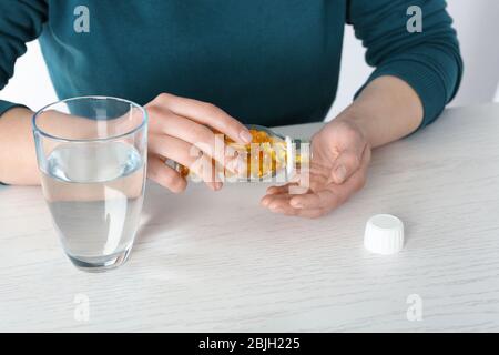 Frau, die Fischöl-Kapseln aus der Flasche in die Hand am Tisch gießt Stockfoto