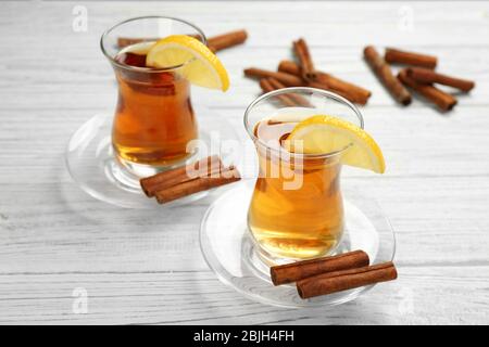 Zwei Glasbecher mit aromatischem heißen Zimttee und Zitrone auf Holztisch Stockfoto