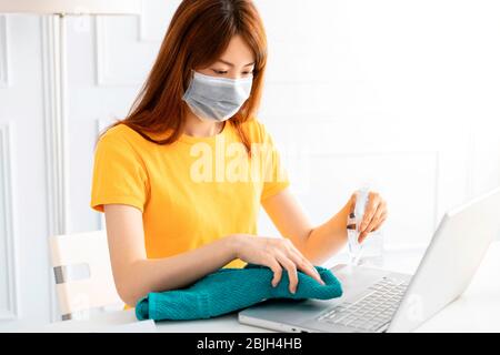 Frau, die Alkohol-Gel zu reinigen Hände und Laptop zu Hause Stockfoto