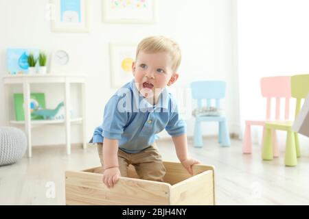 Niedlicher kleiner Junge, der zu Hause in einer Holzkiste steht Stockfoto