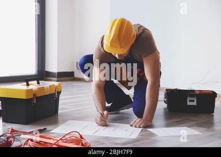 Junger Elektriker prüft Zeichnungen in der Nähe von Werkzeugkästen im hellen Raum Stockfoto