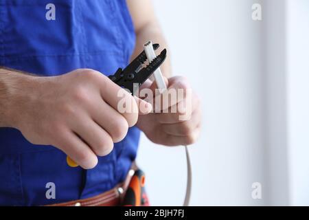 Junger Elektriker enthäuten einen Draht in hellen Raum Stockfoto