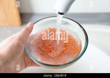 Hand der Frau, die rohe Linsen mit Leitungswasser vor dem Kochen in der Küche wäscht Stockfoto