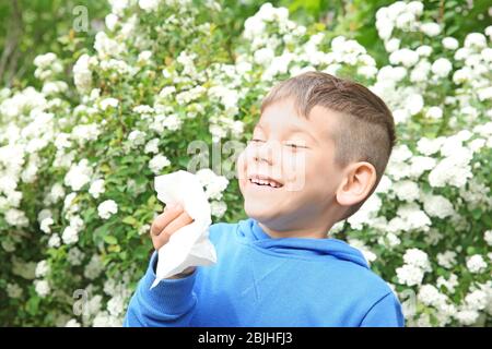 Niesen kleinen niedlichen Jungen mit Nasenwischer unter blühenden Büschen im Park Stockfoto