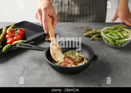 Mann, der Sauce zu geschnittenem Steak in der Pfanne hinzufügt Stockfoto