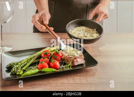 Mann, der Sauce zu geschnittenem Steak mit Gemüse auf dem Teller hinzufügt Stockfoto