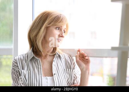Attraktive reife Frau steht in der Nähe von Fenster zu Hause Stockfoto