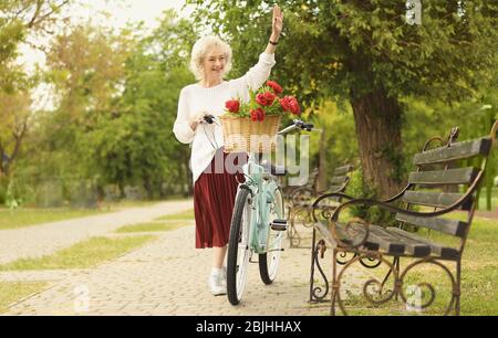 Schöne Frau mittleren Alters winkt ihre Hand im Park Stockfoto