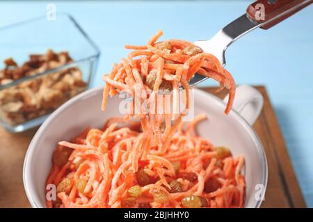 Gabel und Schüssel mit leckeren Karottenrosinensalat auf blauem Tisch Stockfoto