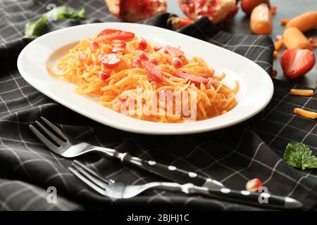 Weißer ovaler Teller mit leckeren Karotten-Erdbeersalat auf schwarz karierter Serviette Stockfoto