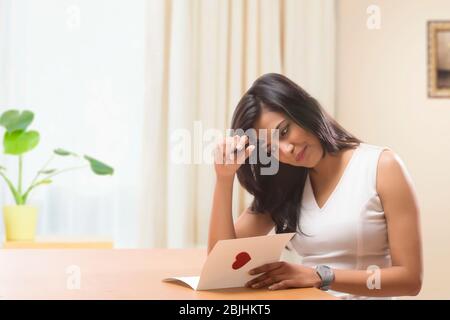 Junge Frau, die zu Hause eine valentinskarte schreibt Stockfoto