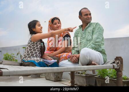 Indische Eltern sitzen auf einem Lager Bett Tochter zeigt etwas Stockfoto