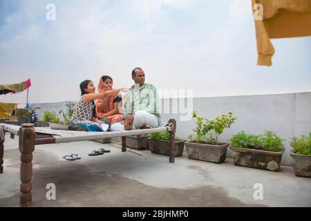 Indische Eltern sitzen auf einem Lager Bett Tochter zeigt etwas Stockfoto