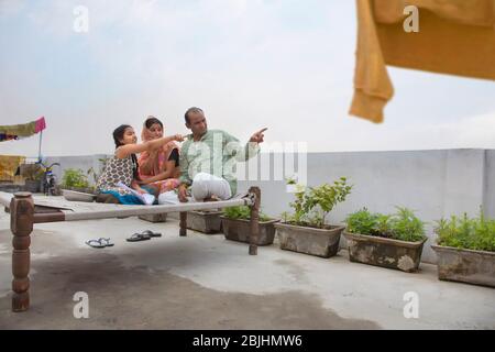 Indische Eltern sitzen zusammen auf einem Lagerbett und zeigen etwas Stockfoto