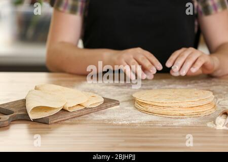 Küchenchef kocht köstliche ungesäuerte Tortillas auf Holztisch Stockfoto