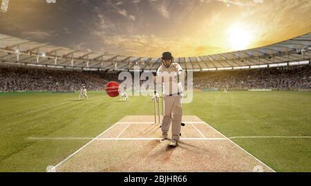 Der junge Sportler schlägt den Ball beim Schlagstock auf dem Cricket-Feld Stockfoto