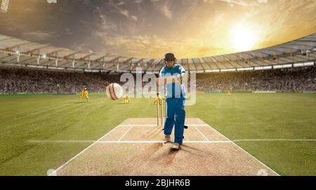 Der junge Sportler schlägt den Ball beim Schlagstock auf dem Cricket-Feld Stockfoto