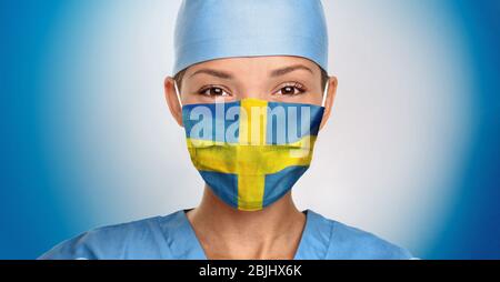 Schweden COVID-19 Ärztin mit Gesichtsmaske mit schwedischer Flagge Print für Coronavirus Hope. Asiatische Krankenschwester Porträt auf blauem Hintergrund. Stockfoto