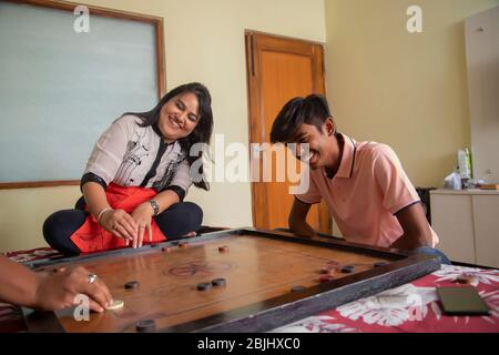 Sohn spielt mit seinen Eltern zu Hause Carrom-Board. Stockfoto