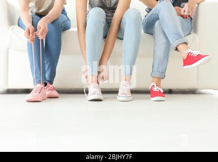 Junge Frauen mit schönen Beinen in Jeans und Turnschuhen sitzen auf dem Sofa Stockfoto