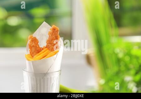 Leckere frittierte Fische und Chips in Papier verpackt, auf verschwommenem Hintergrund Stockfoto
