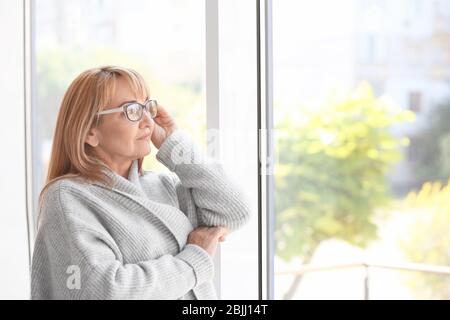 Attraktive reife Frau steht in der Nähe von Fenster zu Hause Stockfoto