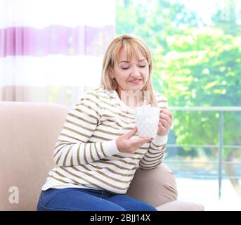 Attraktive, reife Frau auf dem Sofa zu Hause sitzen Stockfoto