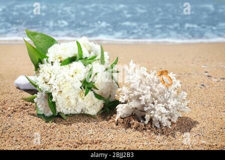 Schönes Bouquet und goldene Ringe an Korallen am Meer. Hochzeitskonzept am Strand Stockfoto