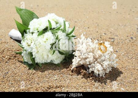 Schönes Bouquet und goldene Ringe an Korallen am Meer. Hochzeitskonzept am Strand Stockfoto