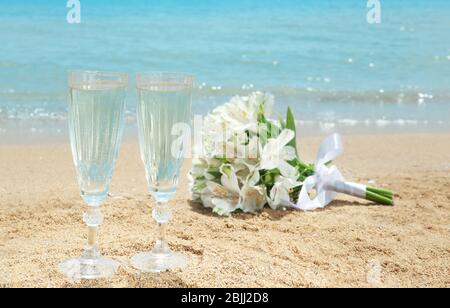Gläser mit Champagner und schönem Bouquet auf Sand. Hochzeitskonzept am Strand Stockfoto