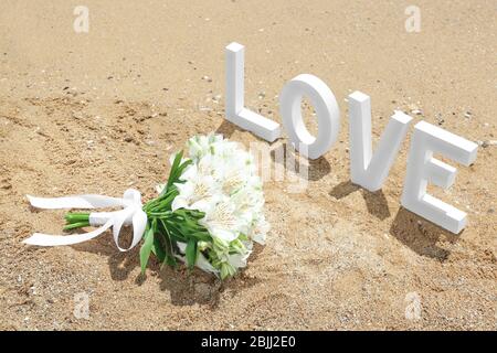 Schöner Strauß und WORTLIEBE auf Sand. Hochzeitskonzept am Strand Stockfoto