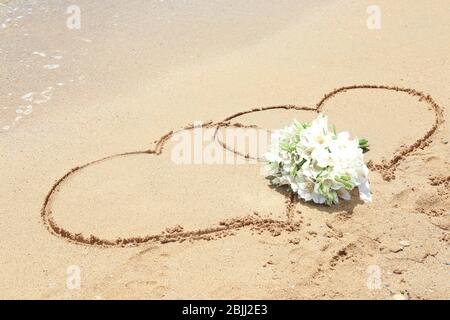 Schöner Strauß und Herzzeichnen auf Sand. Hochzeitskonzept am Strand Stockfoto