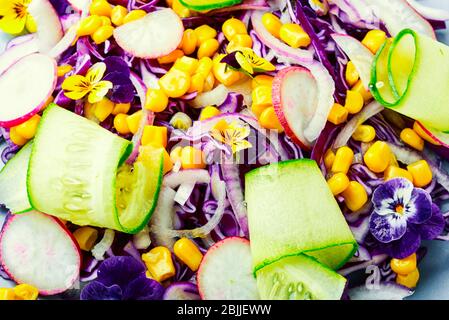 Salat mit Rotkohl, Rettich, Mais, Gurke und Blumen.Frühlingssalat mit essbaren Blumen dekoriert. Stockfoto