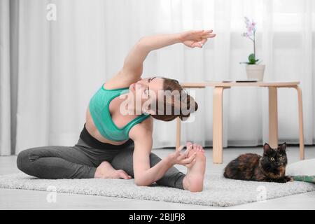 Junge schöne Frau mit Katze Yoga zu Hause üben Stockfoto