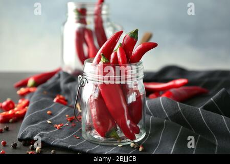 Rote Chilischoten im Glasgefäß auf schwarz gestreiftem Stoff Stockfoto