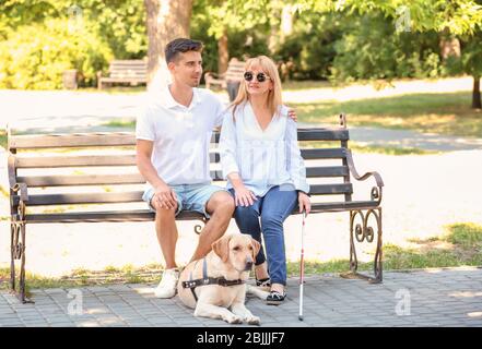 Junger Mann und blinde Frau mit Blindenhund auf Bank im Park sitzen Stockfoto