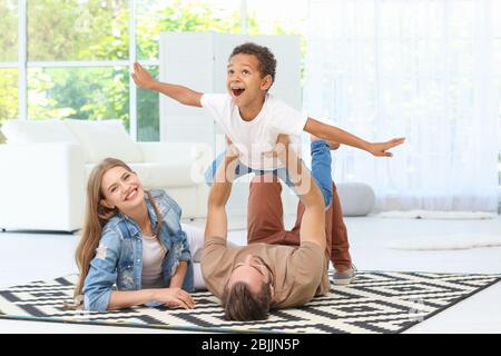 Glückliches Paar spielt mit adoptierten afroamerikanischen Jungen auf Teppich zu Hause Stockfoto