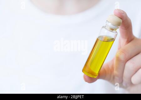 Das Mädchen hält in der Hand eine transparente Flasche mit Öl auf einem hellen Hintergrund. Aromatisches Öl, ätherisches Öl. Nahaufnahme. Platz für Text. Modell Stockfoto