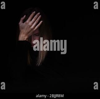 Junge kaukasische Frau, die sich in Selbstisolation traurig und depressiv fühlt, unter psychischer Gesundheit leidet, vor schwarzem Hintergrund. Stockfoto
