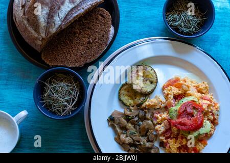 Mexikanische Eier mit Brot, Pilzen und Zucchini, auf weißem Teller auf blauem Tisch. Stockfoto