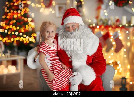 Kleines Mädchen auf Santa's Schoß im Zimmer mit schönen Weihnachtsdekorationen sitzen Stockfoto