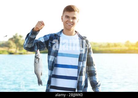 Junger Mann hält frisch gefangenen Fisch in der Nähe des Flusses Stockfoto