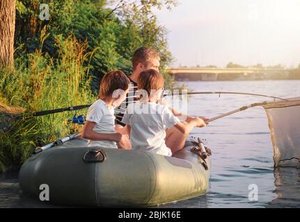 Vater mit Söhnen, die vom Boot aus auf dem Fluss fischen Stockfoto