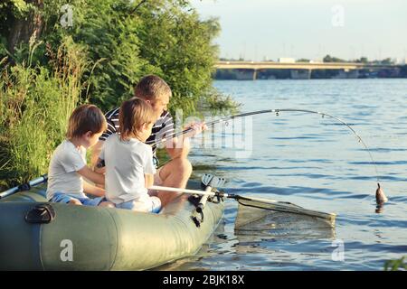 Vater mit Söhnen, die vom Boot aus auf dem Fluss fischen Stockfoto