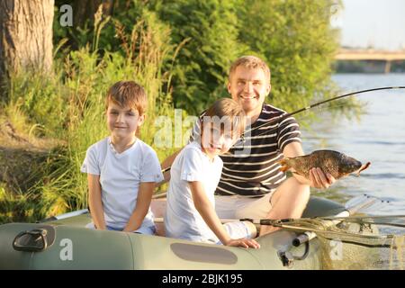 Vater mit Söhnen, die vom Boot aus auf dem Fluss fischen Stockfoto