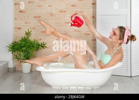 Lustige junge Frau spielt mit Gießkanne in der Badewanne zu Hause Stockfoto