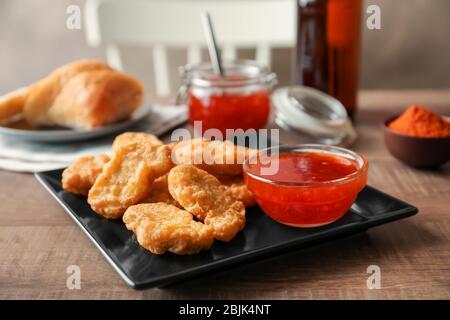 Teller mit Hähnchennuggets und Chilisauce auf Küchentisch Stockfoto