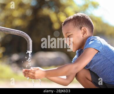 Afroamerikanisches Kind Trinkwasser aus dem Wasserhahn im Freien. Konzept der Wasserknappheit Stockfoto